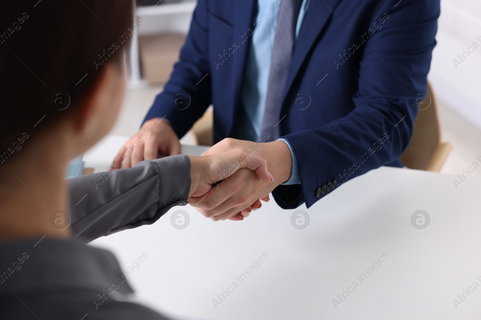 Photo of Business partners shaking hands at table indoors, closeup