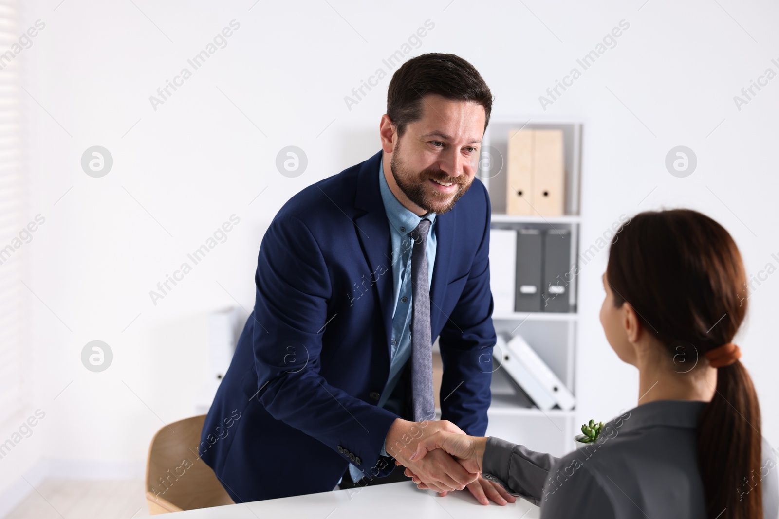 Photo of Business partners shaking hands at table indoors