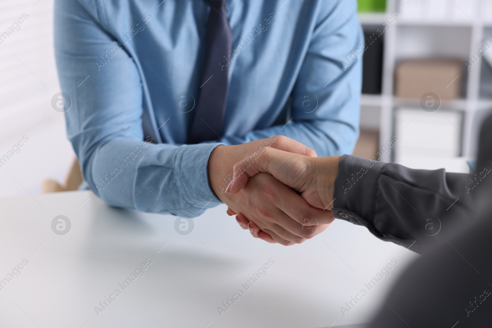 Photo of Business partners shaking hands at table indoors, closeup