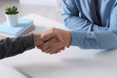 Photo of Business partners shaking hands at table indoors, closeup
