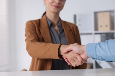 Photo of Business partners shaking hands at table indoors, closeup