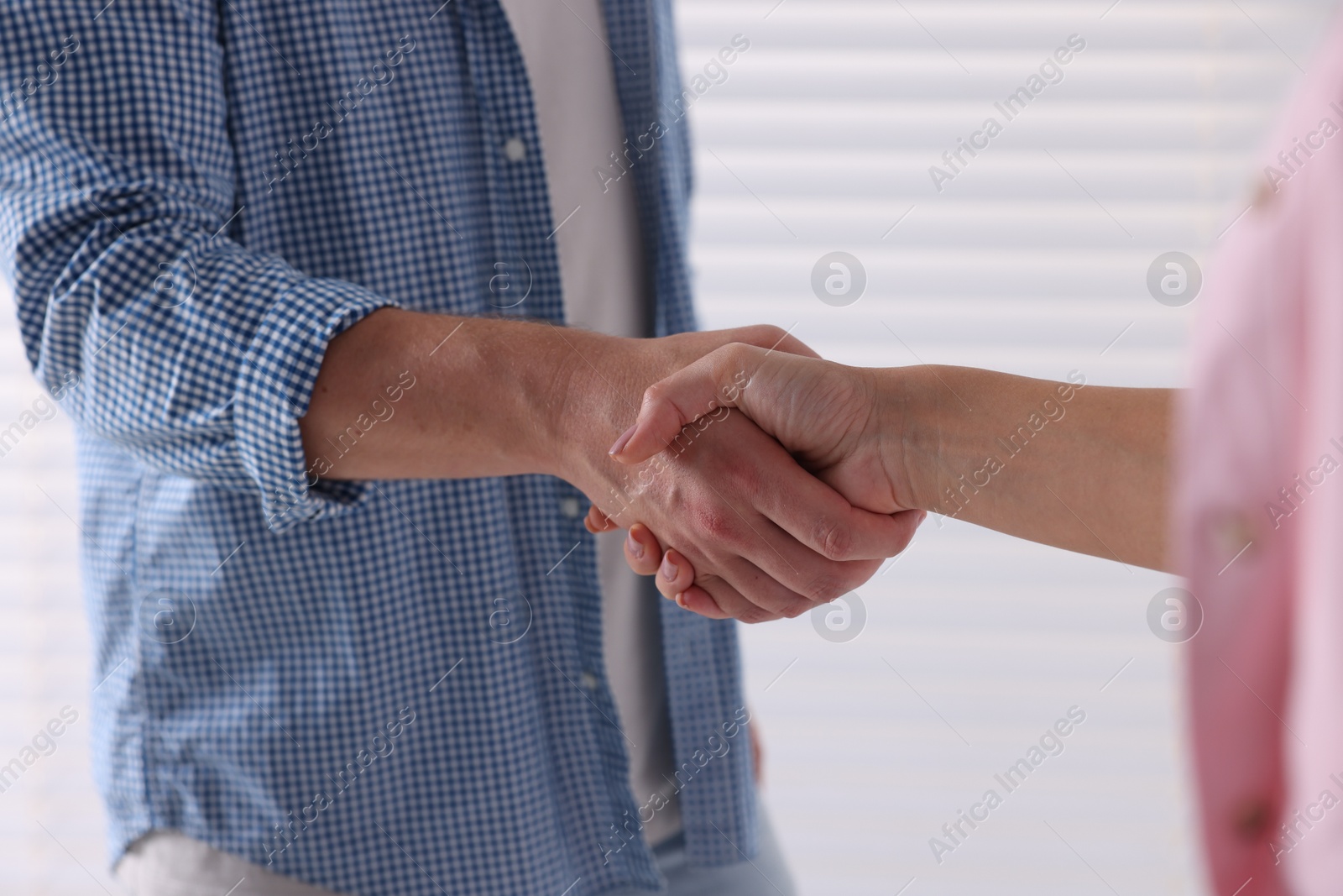 Photo of Man and woman shaking hands near window indoors, closeup