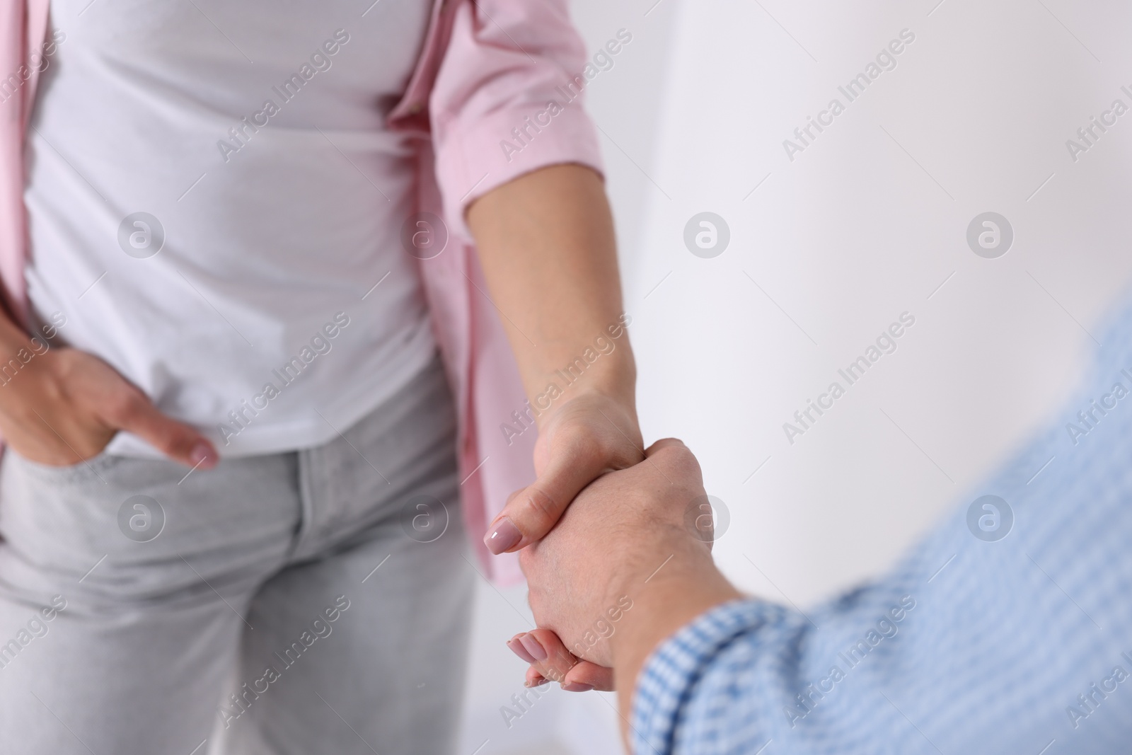 Photo of Man and woman shaking hands near window indoors, closeup