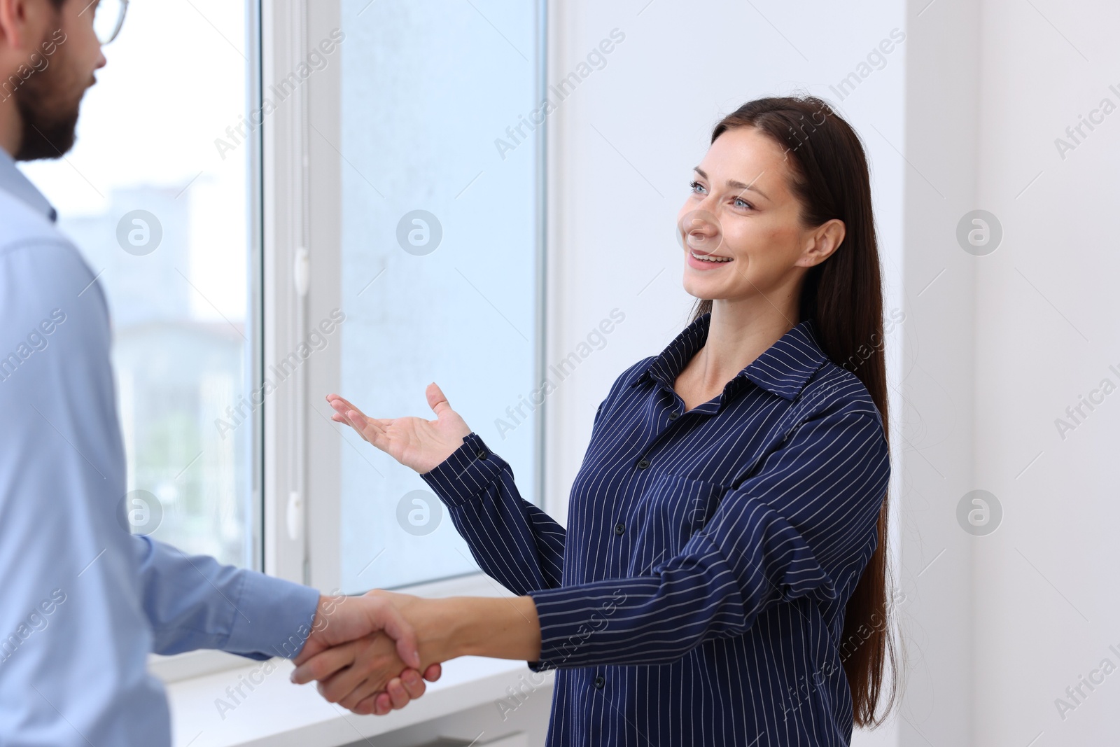 Photo of Man and woman shaking hands near window indoors