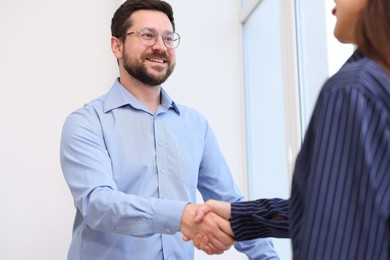 Photo of Man and woman shaking hands near window indoors, low angle view