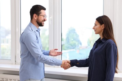 Photo of Man and woman shaking hands near window indoors