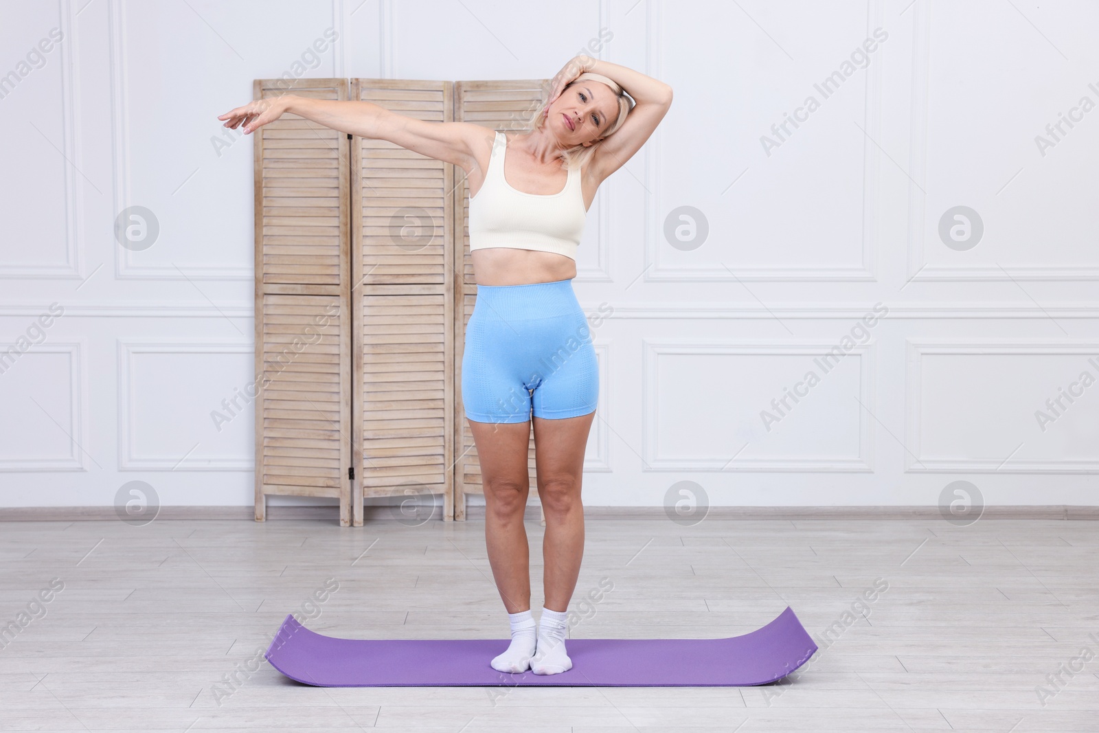 Photo of Mature woman in sportswear stretching on mat at home