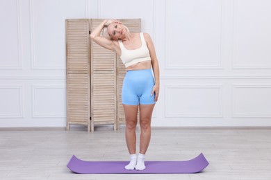 Photo of Mature woman in sportswear stretching on mat at home