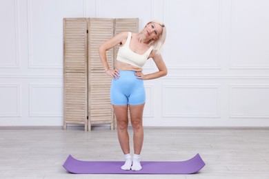 Photo of Mature woman in sportswear stretching on mat at home