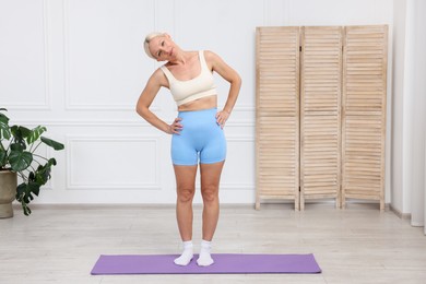 Photo of Mature woman in sportswear stretching on mat at home