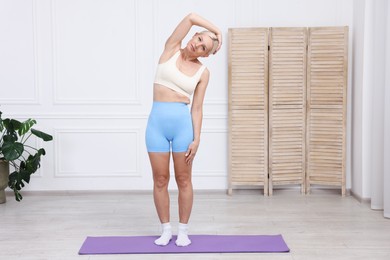 Photo of Mature woman in sportswear stretching on mat at home