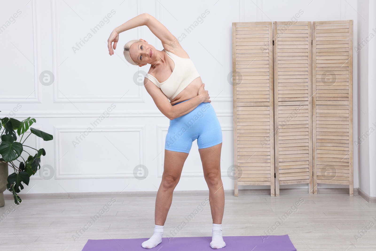 Photo of Mature woman in sportswear stretching on mat at home