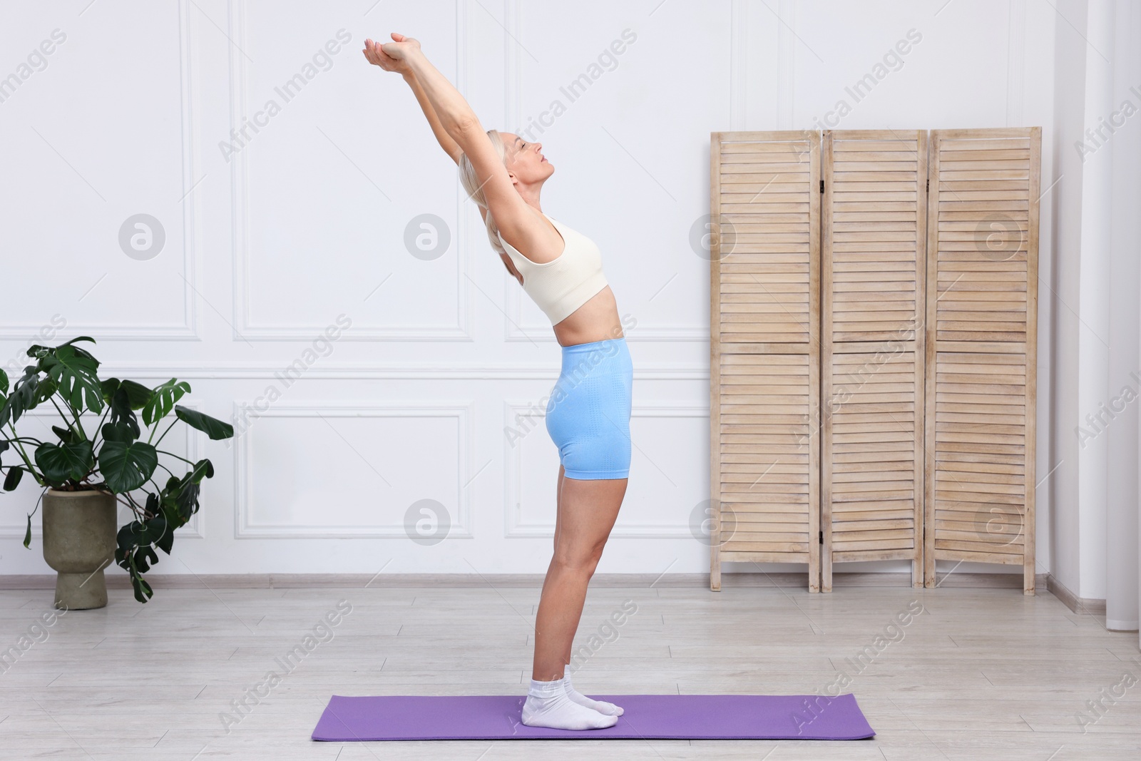 Photo of Mature woman in sportswear stretching on mat at home