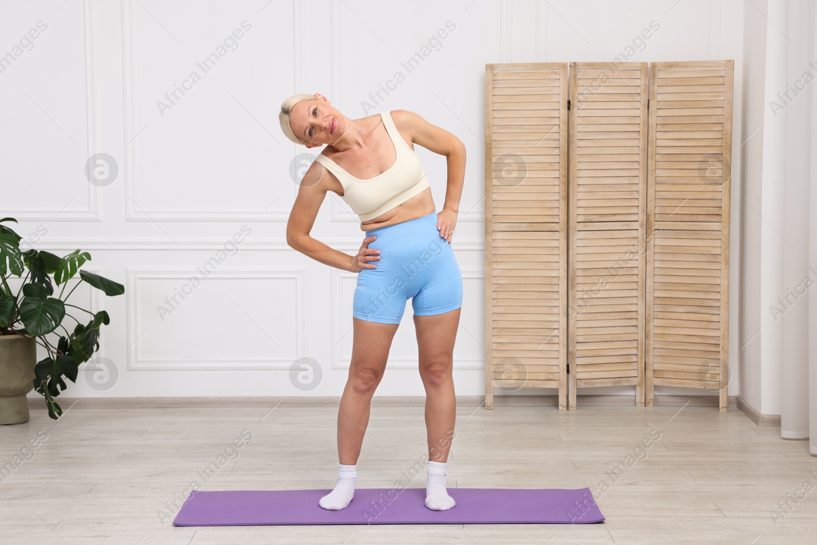 Photo of Mature woman in sportswear stretching on mat at home