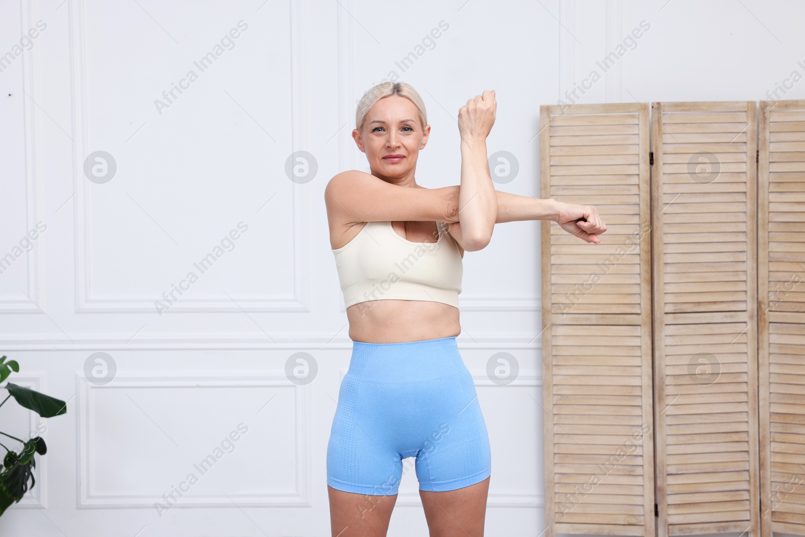 Photo of Mature woman in sportswear stretching at home