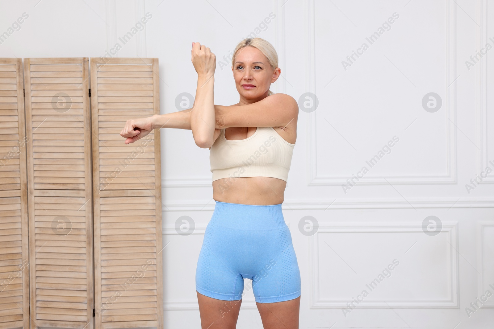 Photo of Mature woman in sportswear stretching at home