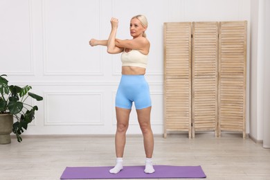 Photo of Mature woman in sportswear stretching on mat at home