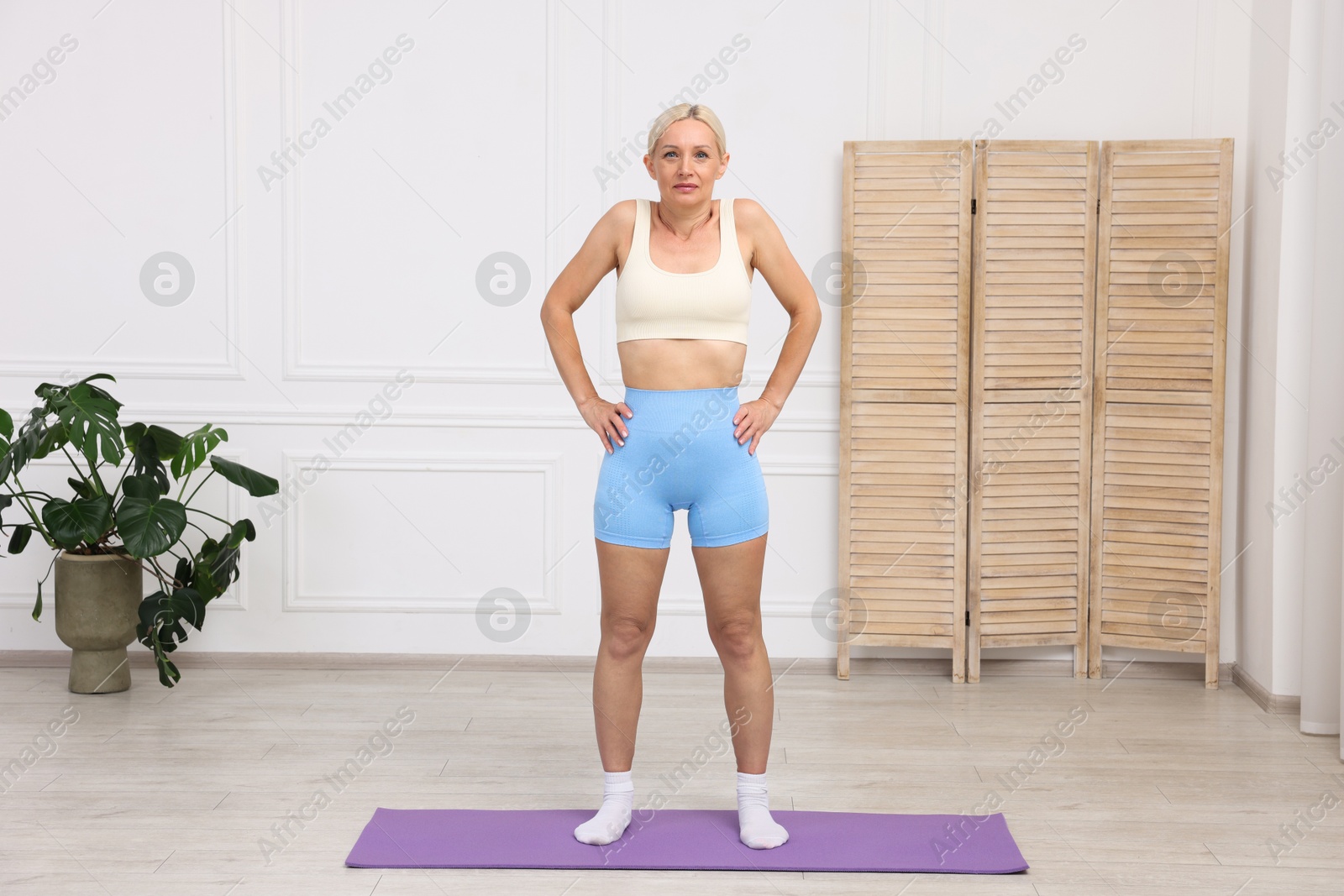 Photo of Mature woman in sportswear stretching on mat at home
