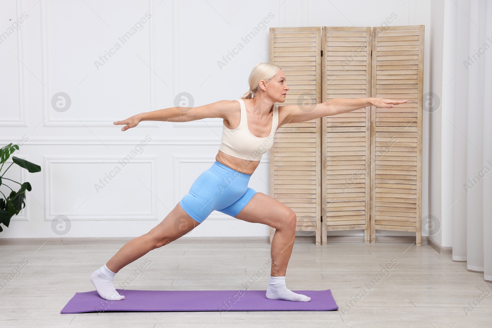 Photo of Mature woman in sportswear stretching on mat at home