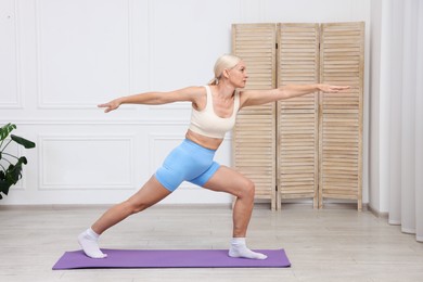 Photo of Mature woman in sportswear stretching on mat at home