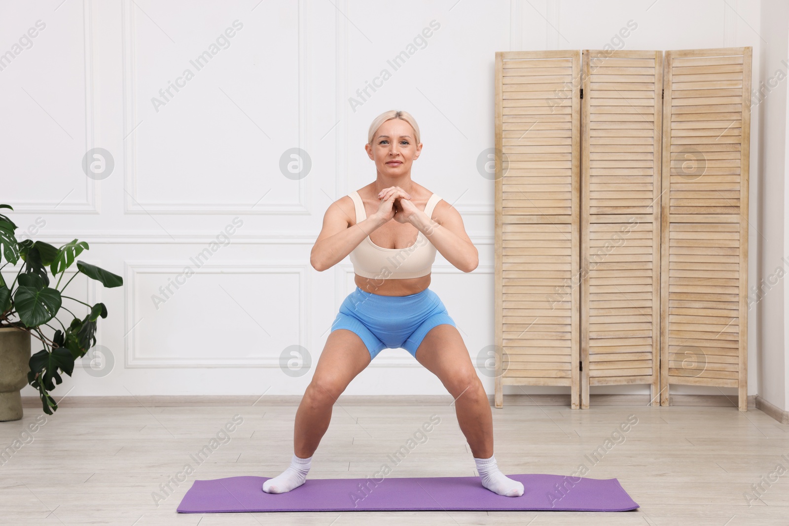 Photo of Mature woman in sportswear stretching on mat at home
