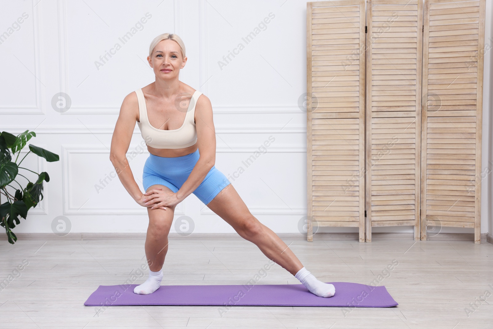 Photo of Mature woman in sportswear stretching on mat at home