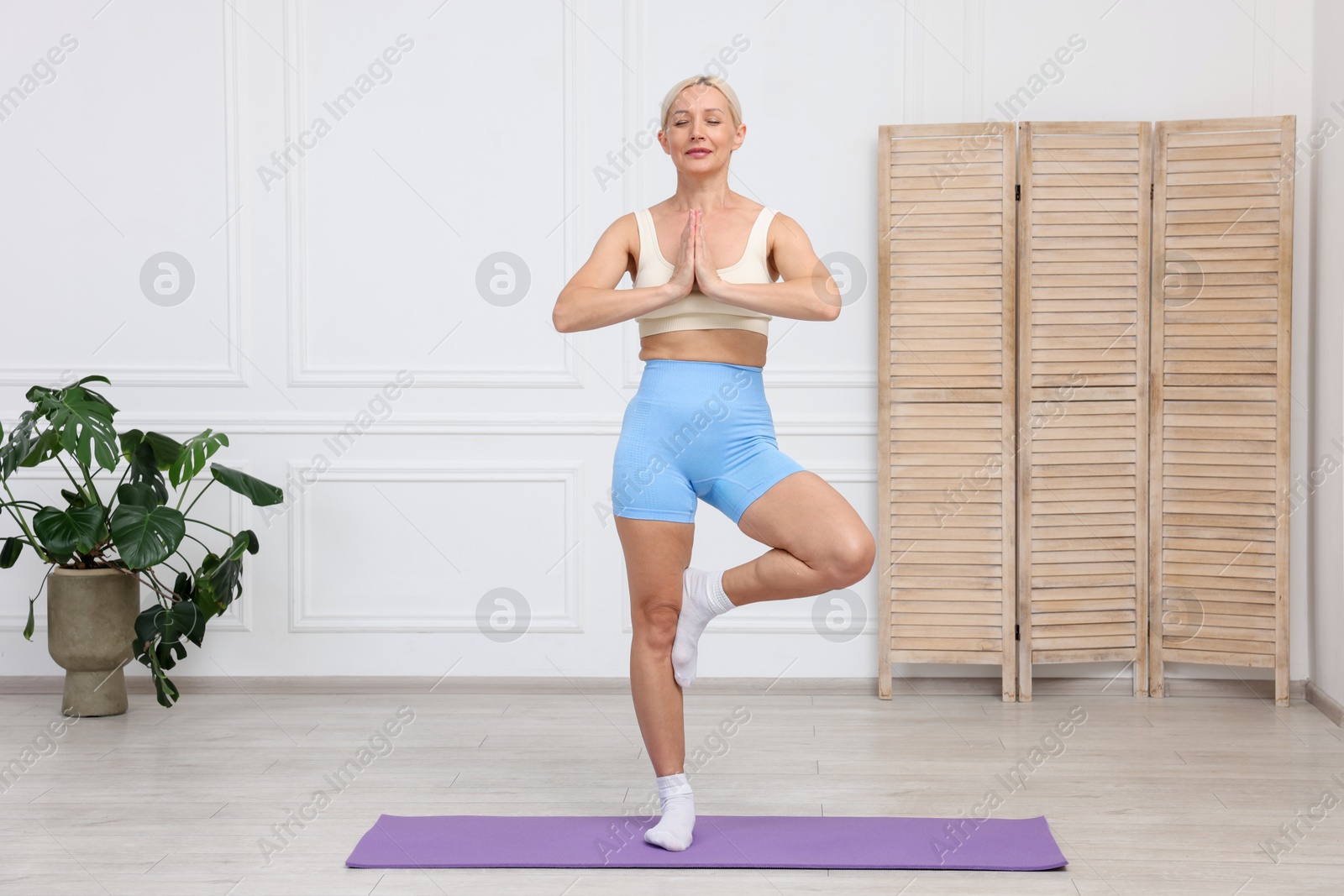 Photo of Mature woman in sportswear practicing yoga on mat at home. Stretching