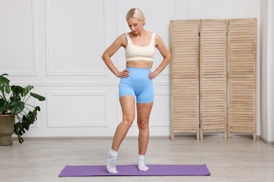 Photo of Mature woman in sportswear doing morning exercise on mat at home. Stretching