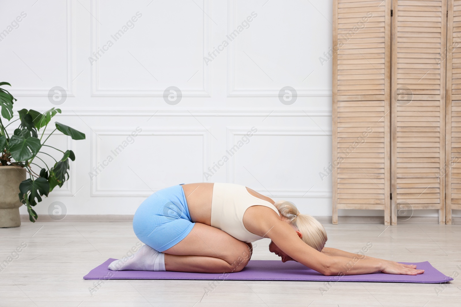 Photo of Mature woman in sportswear stretching on mat at home