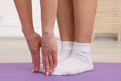 Photo of Mature woman stretching on mat at home, closeup