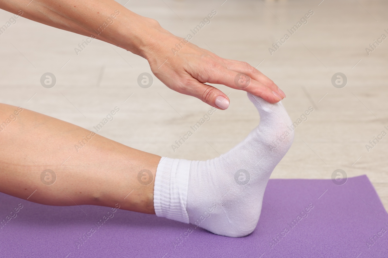 Photo of Mature woman stretching on mat at home, closeup