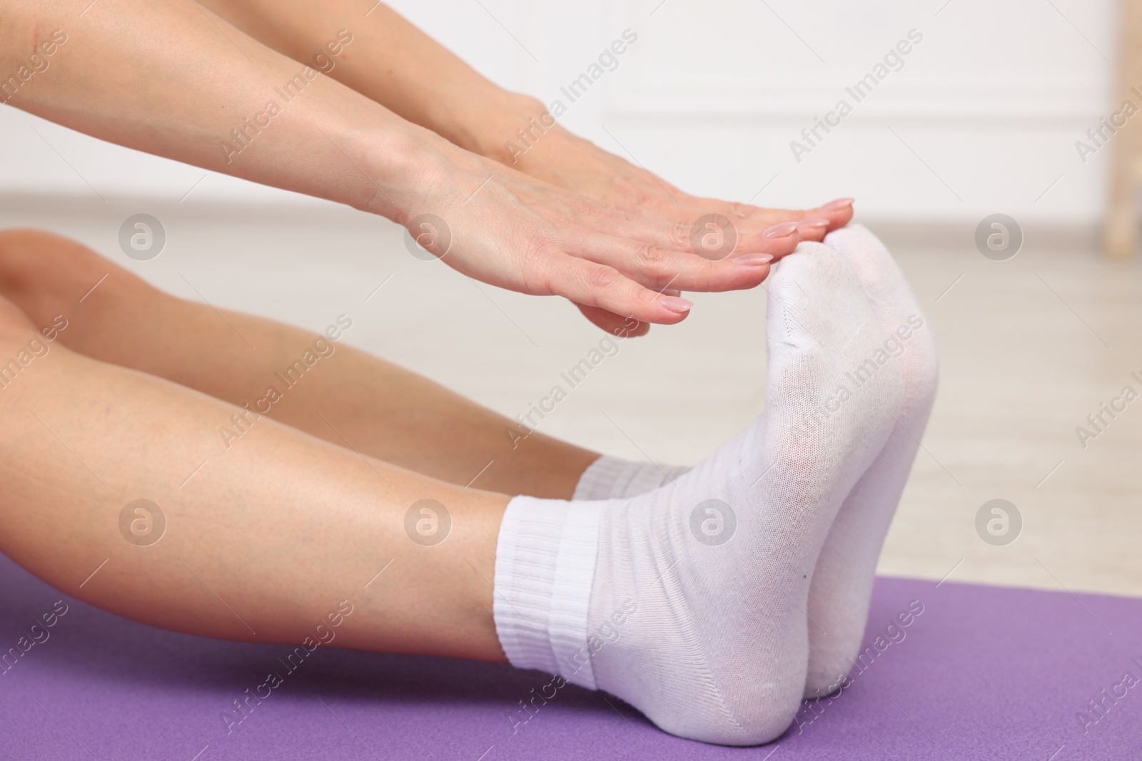 Photo of Mature woman stretching on mat at home, closeup