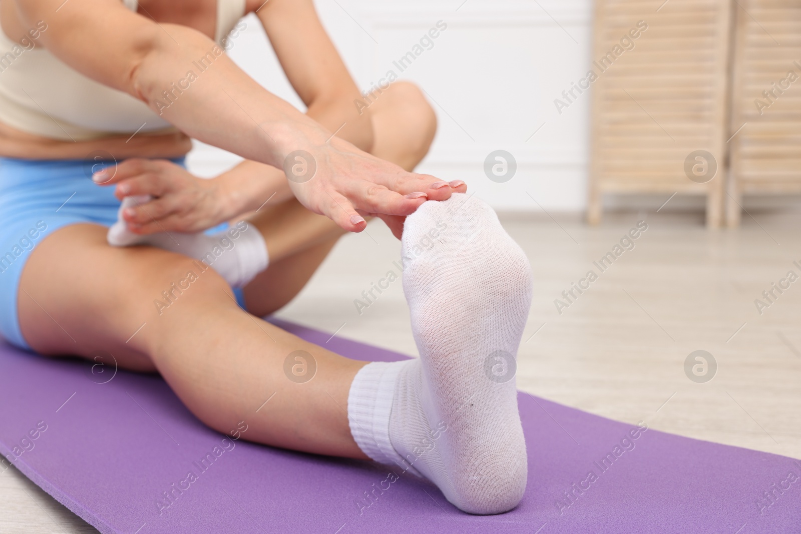 Photo of Mature woman stretching on mat at home, closeup
