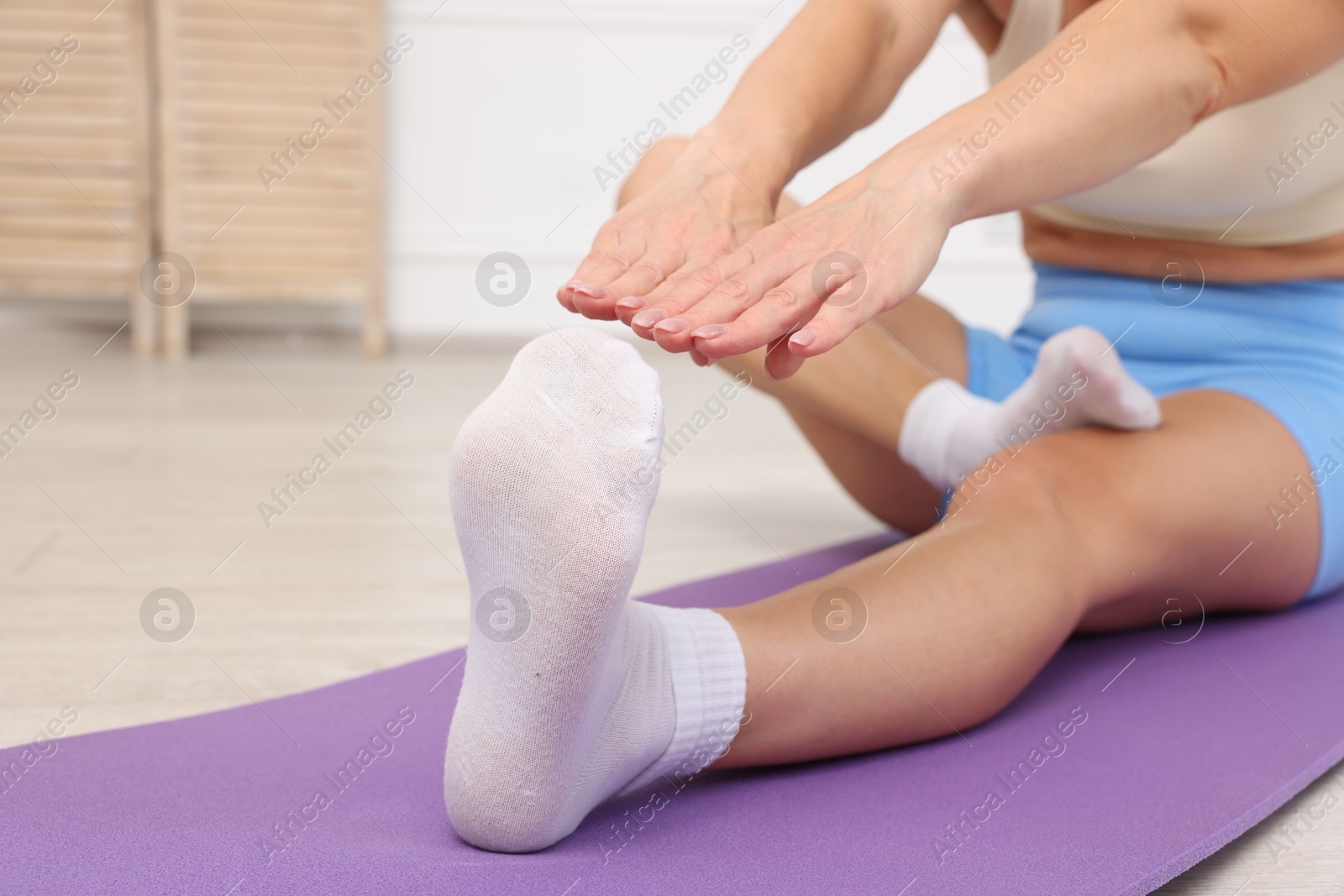 Photo of Mature woman stretching on mat at home, closeup