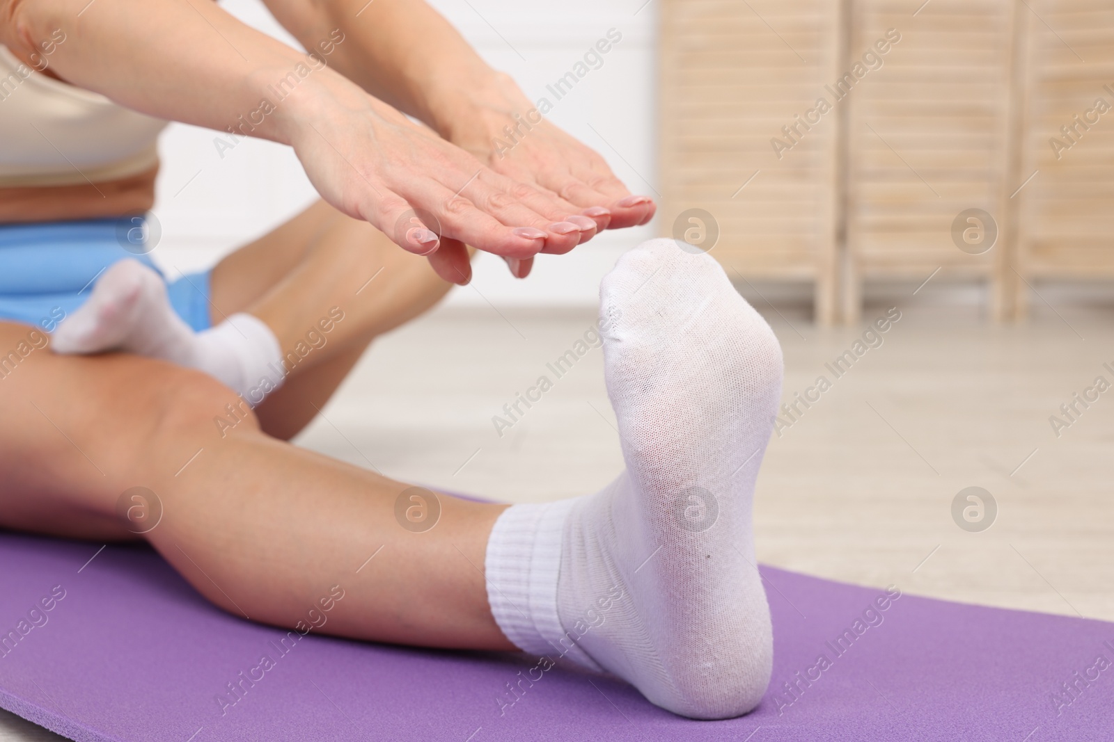 Photo of Mature woman stretching on mat at home, closeup