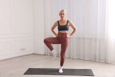 Photo of Mature woman in sportswear stretching on mat near window at home
