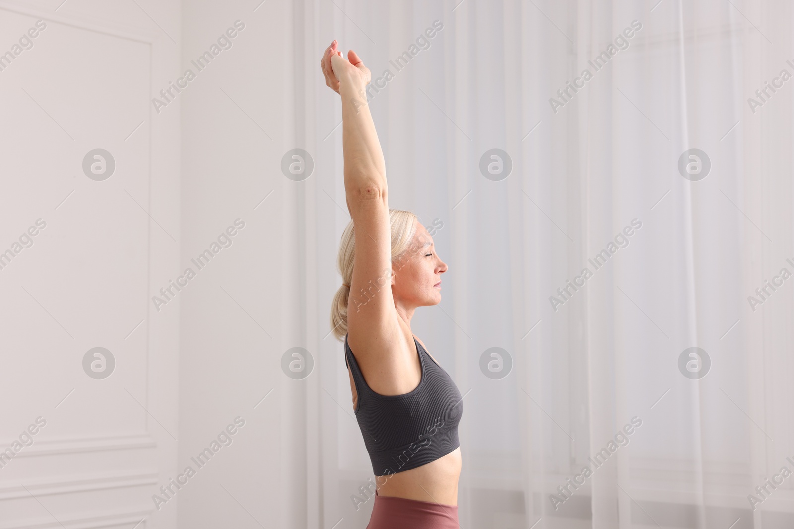 Photo of Mature woman in sportswear stretching near window at home