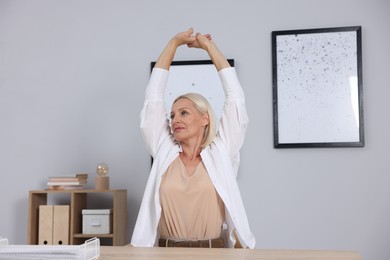 Photo of Mature woman stretching at table near grey wall