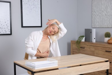Photo of Mature woman stretching at table near grey wall