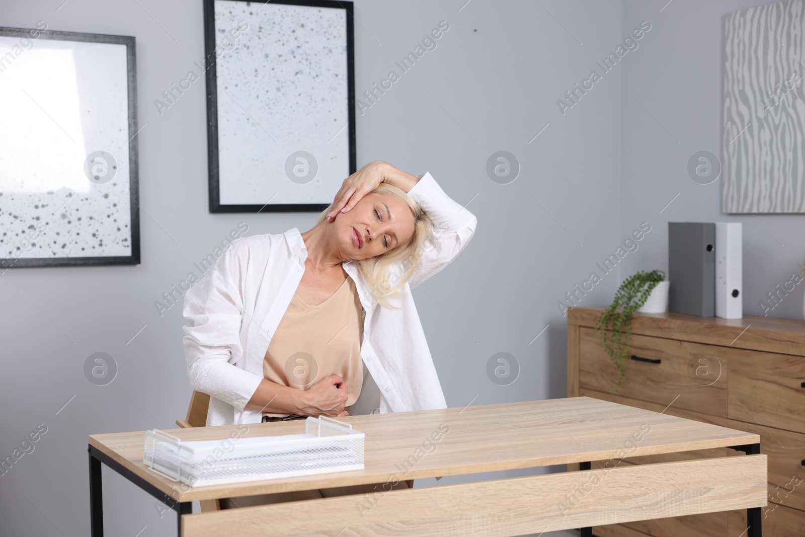 Photo of Mature woman stretching at table near grey wall
