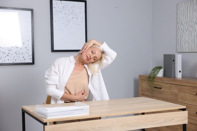 Photo of Mature woman stretching at table near grey wall