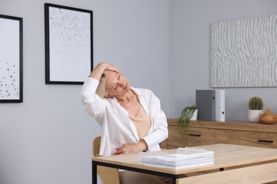 Photo of Mature woman stretching at table near grey wall