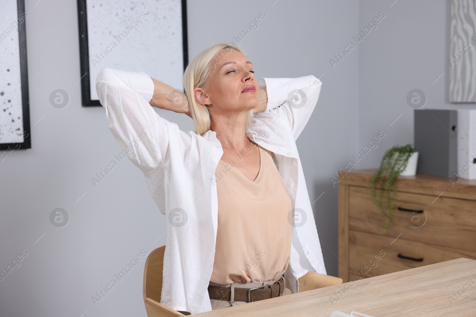 Photo of Mature woman stretching at workplace near grey wall