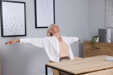 Photo of Mature woman stretching at table near grey wall