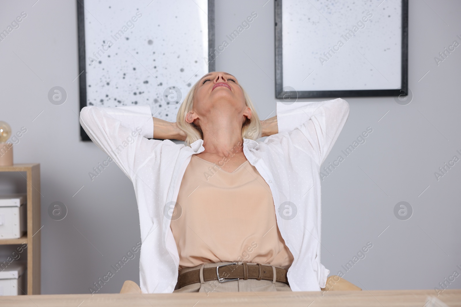 Photo of Mature woman stretching at workplace near grey wall