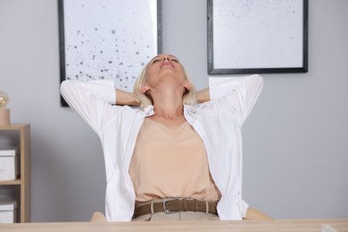 Photo of Mature woman stretching at workplace near grey wall