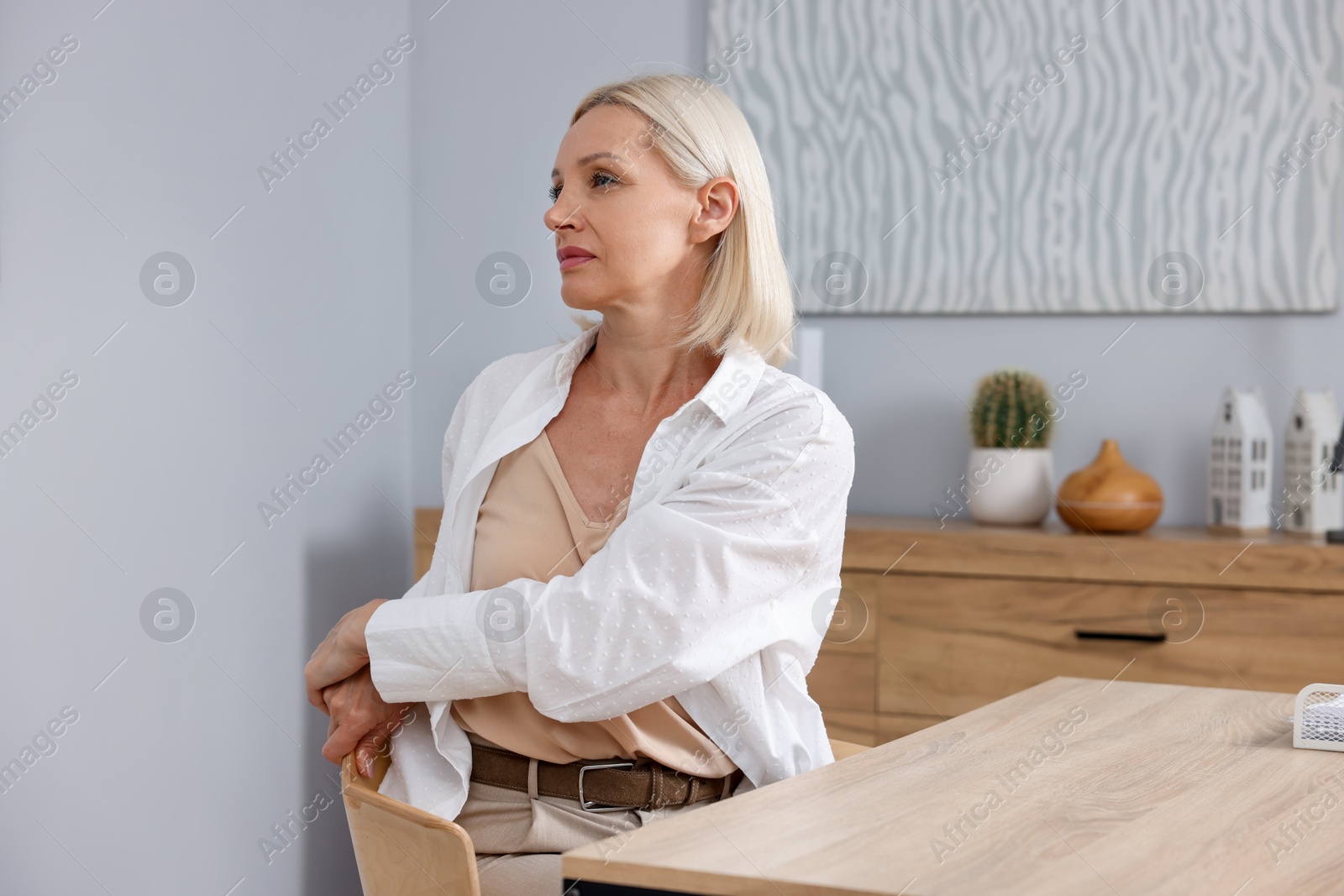 Photo of Mature woman stretching at table near grey wall