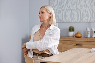 Photo of Mature woman stretching at table near grey wall