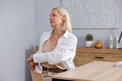 Photo of Mature woman stretching at table near grey wall