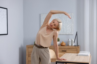 Photo of Mature woman stretching leaning on table in office